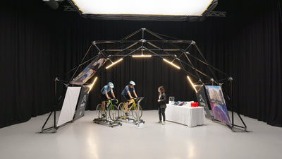 Configuración interior de la estructura para eventos de Konligo con dos ciclistas en bicicletas estáticas y una mesa de exhibición con cascos y botellas de agua. Ahora disponible en MTN Shop EE. UU.