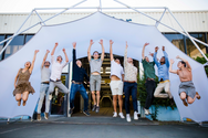 Group of people jumping in front of a Konligo Fastival event structure with a white membrane cover, celebrating outside a modern industrial building, now available on MTN Shop US. - imagen 9